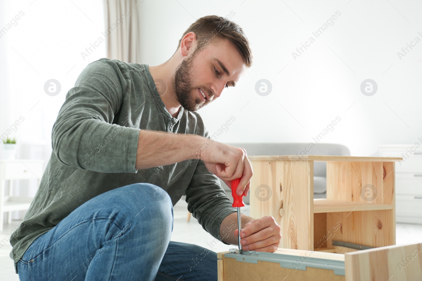 Photo of Young working man repairing drawer at home