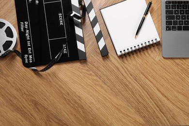 Movie clapper, film reel, notebook and laptop on wooden table, flat lay. Space for text