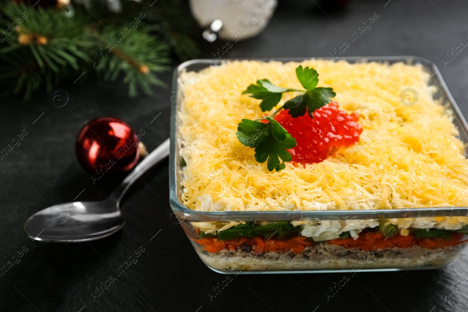 Photo of Traditional russian salad Mimosa and festive decor on black table, closeup