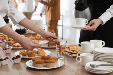 People near table with dishware and different delicious snacks during coffee break, closeup