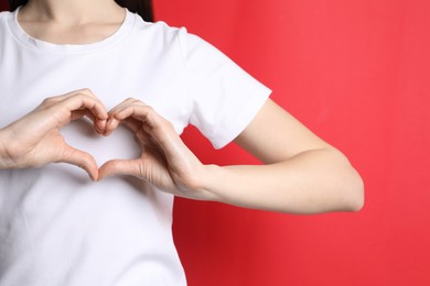 Photo of Woman making heart with hands on red background, closeup