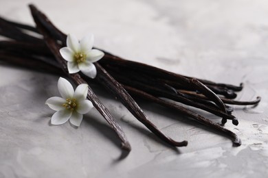 Photo of Vanilla pods and flowers on light textured table, closeup