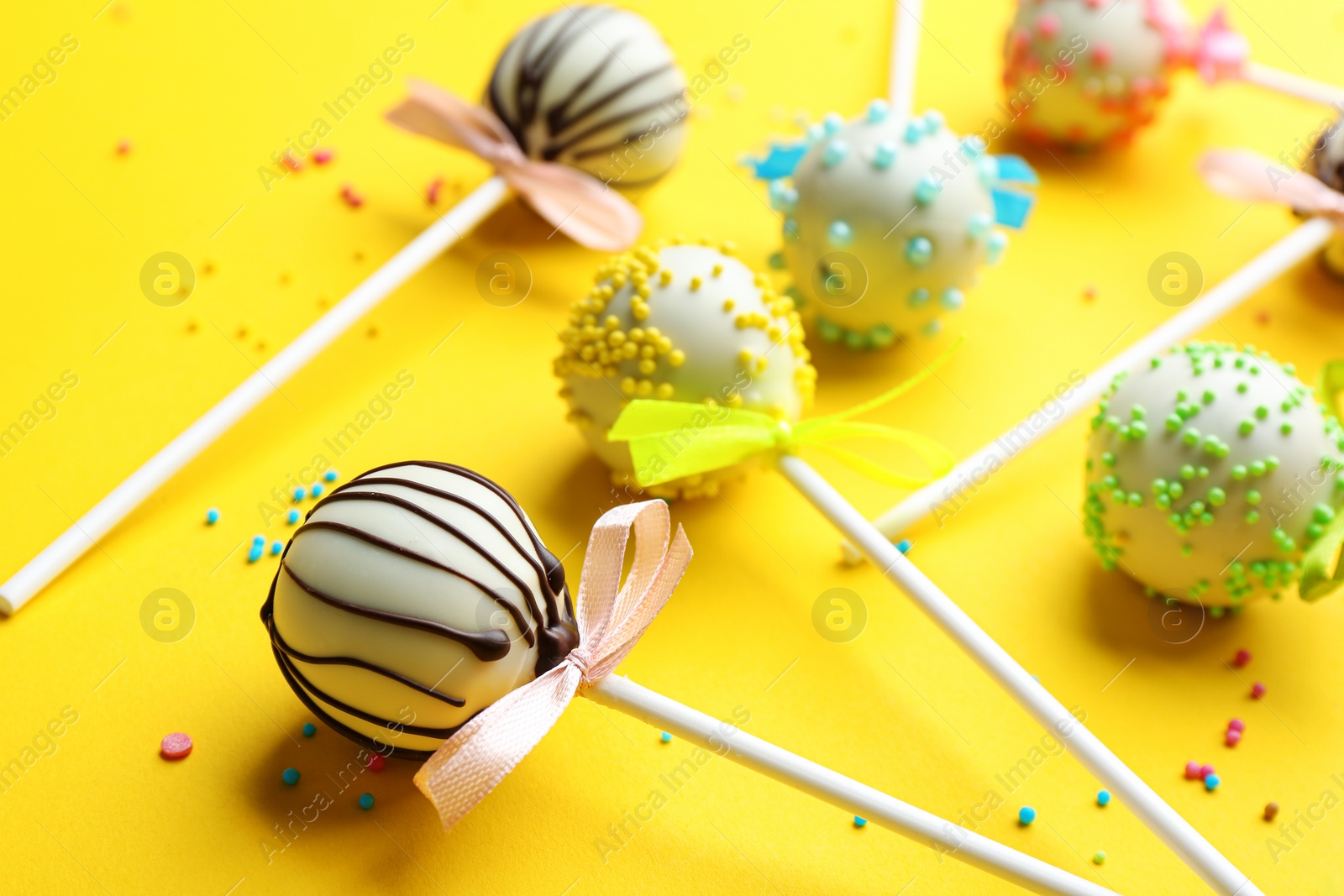 Photo of Different tasty cake pops with sprinkles on yellow background