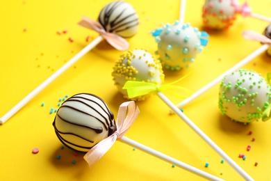 Different tasty cake pops with sprinkles on yellow background