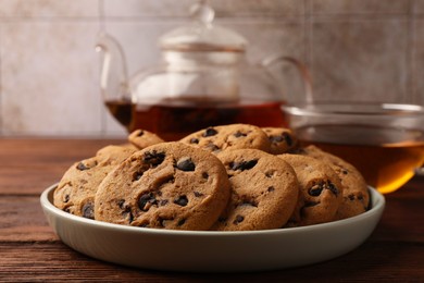 Photo of Delicious chocolate chip cookies and tea on wooden table, closeup