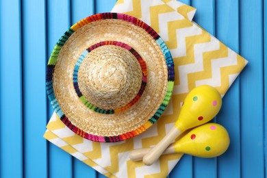 Mexican sombrero hat, towel and maracas on blue wooden surface, top view