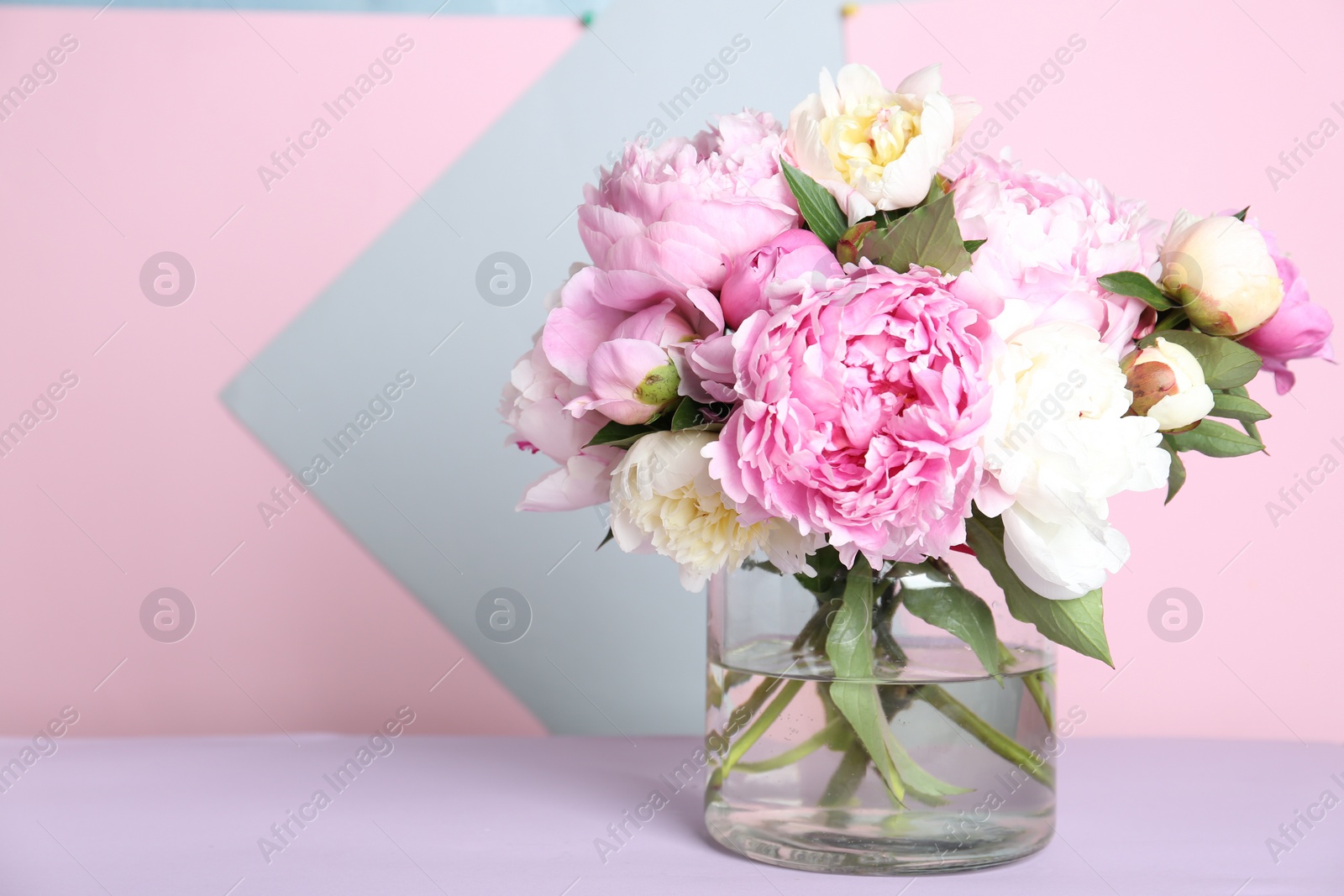 Photo of Bouquet of beautiful peonies in vase on lilac table. Space for text