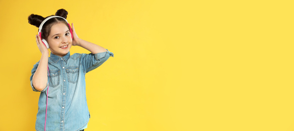 Image of Little girl listening to music with headphones on yellow background, space for text. Banner design