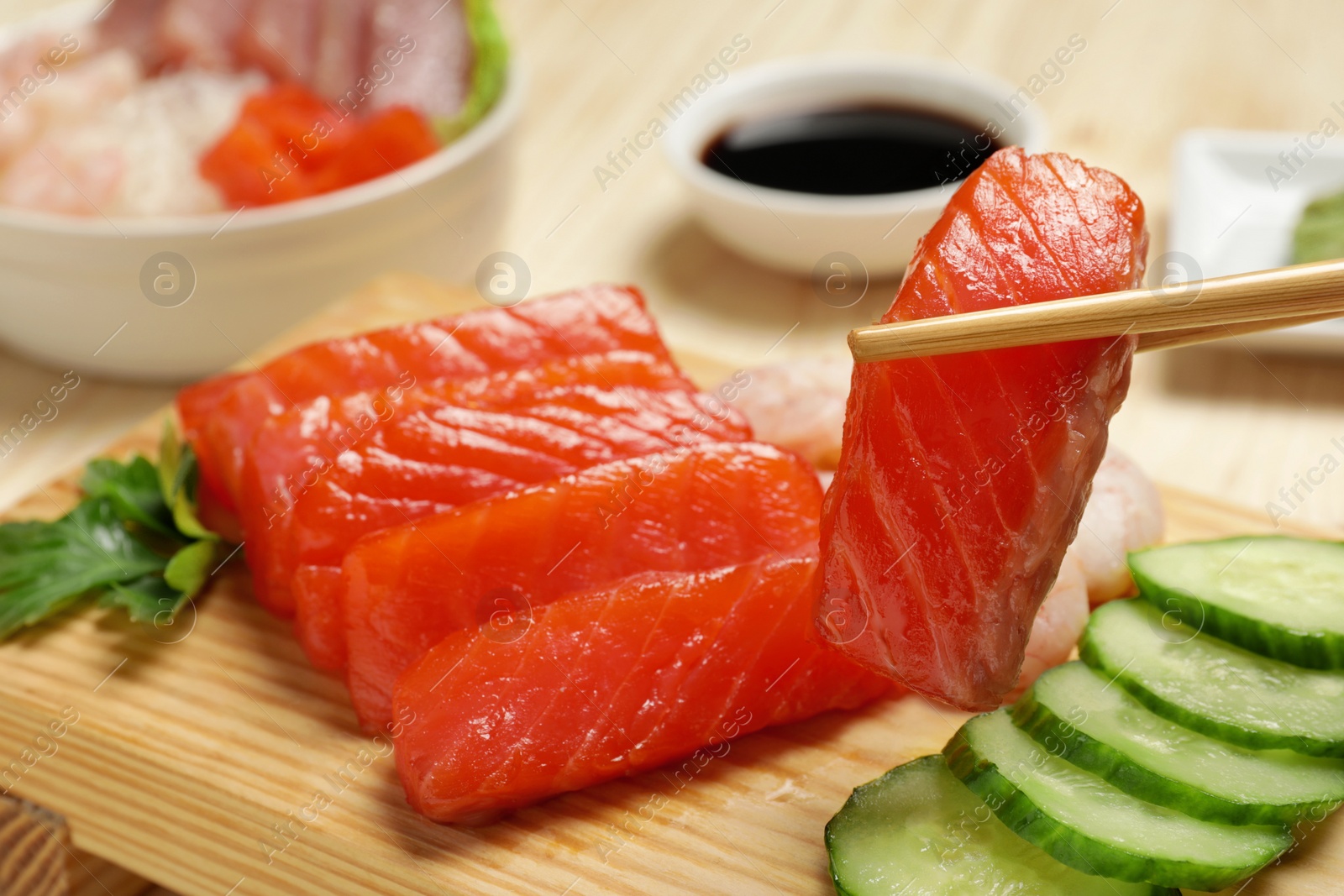 Photo of Taking delicious piece of salmon from serving board at table, closeup. Tasty sashimi dish