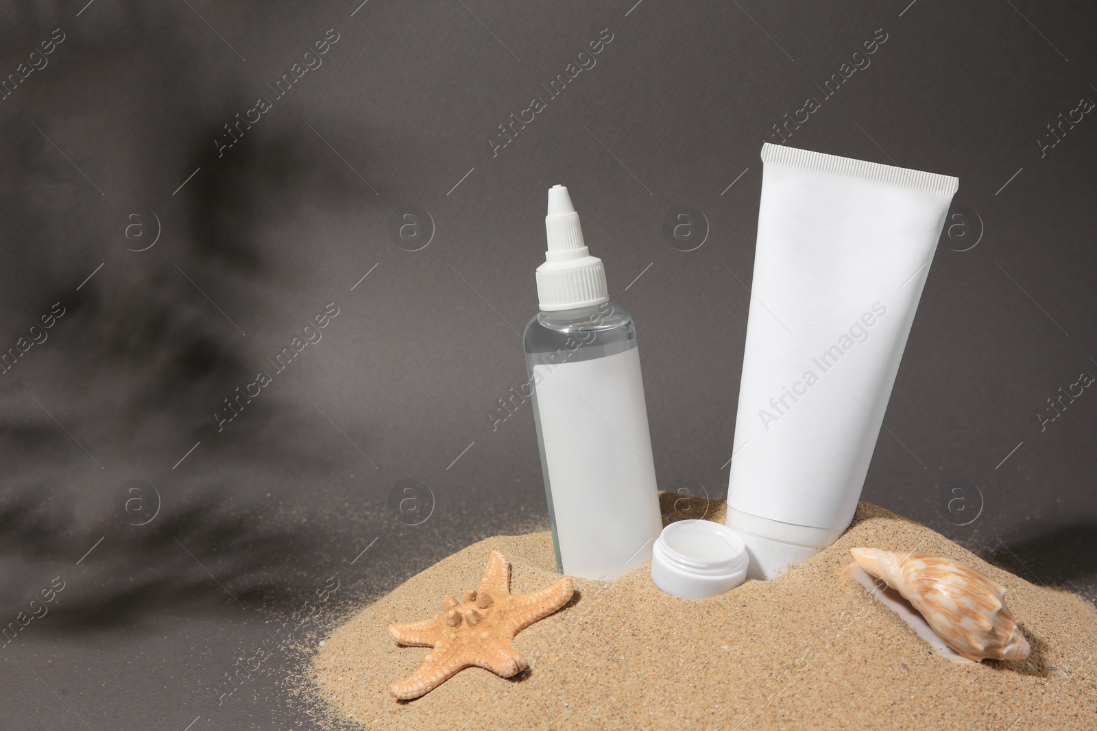 Photo of Cosmetic products, starfish and seashell on sand against grey background. Space for text