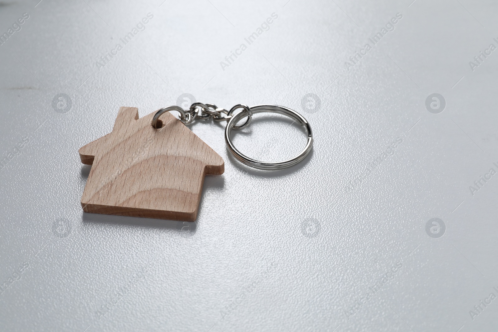Photo of Wooden keychain in shape of house on light table, closeup. Space for text