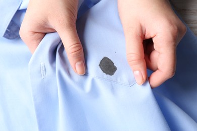 Photo of Woman holding shirt with black ink stain, top view