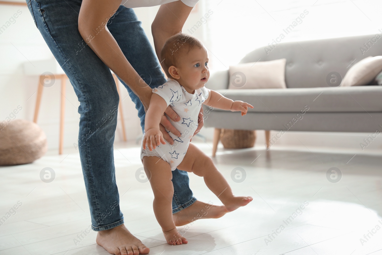 Photo of Father supporting his baby daughter while she learning to walk at home