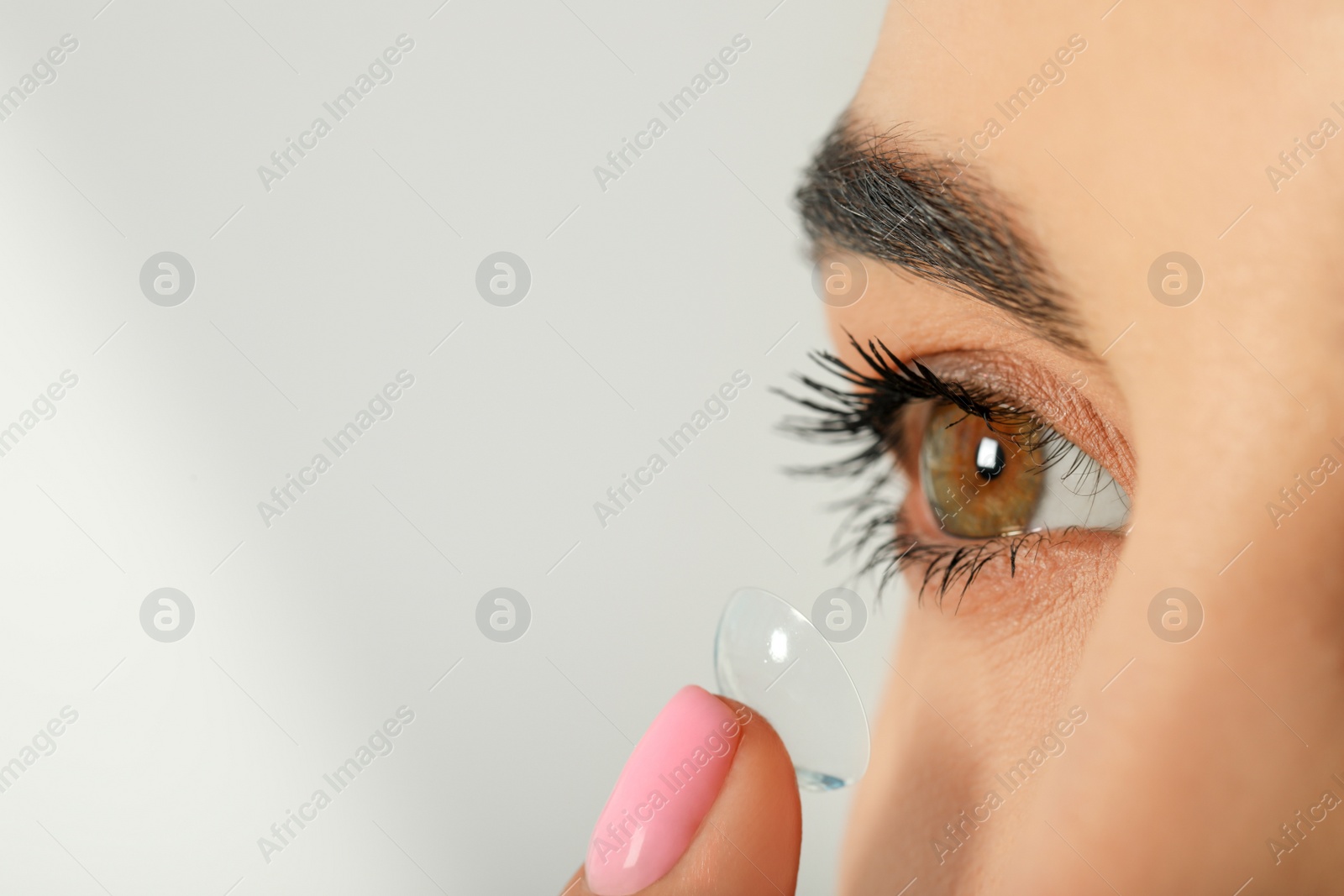 Photo of Young woman putting contact lens in her eye, closeup. Space for text