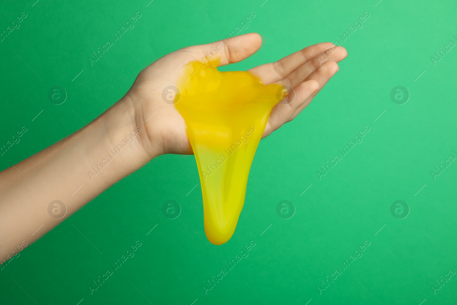 Photo of Woman playing with yellow slime on green background, closeup. Antistress toy