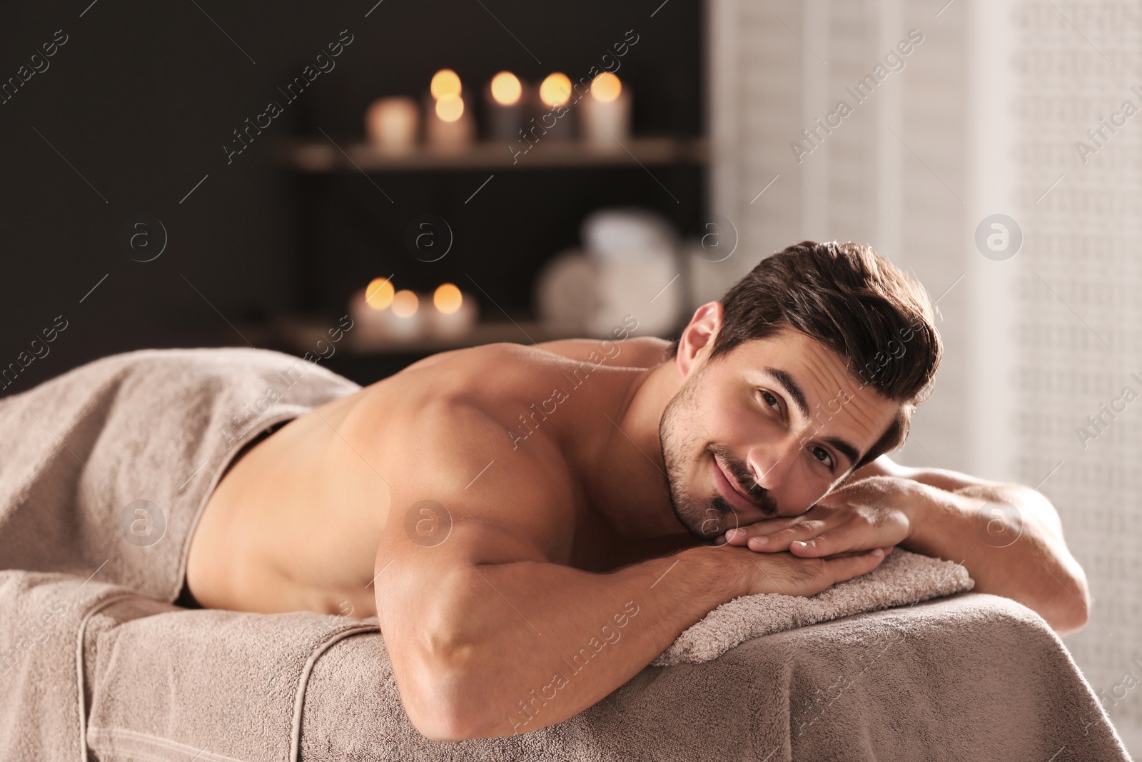 Photo of Handsome young man relaxing on massage table in spa salon, space for text