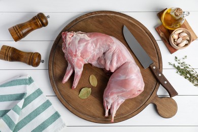 Whole raw rabbit, spices and knife at white wooden table, flat lay