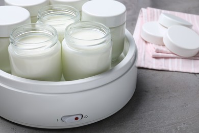 Photo of Modern yogurt maker with full jars on grey table, closeup