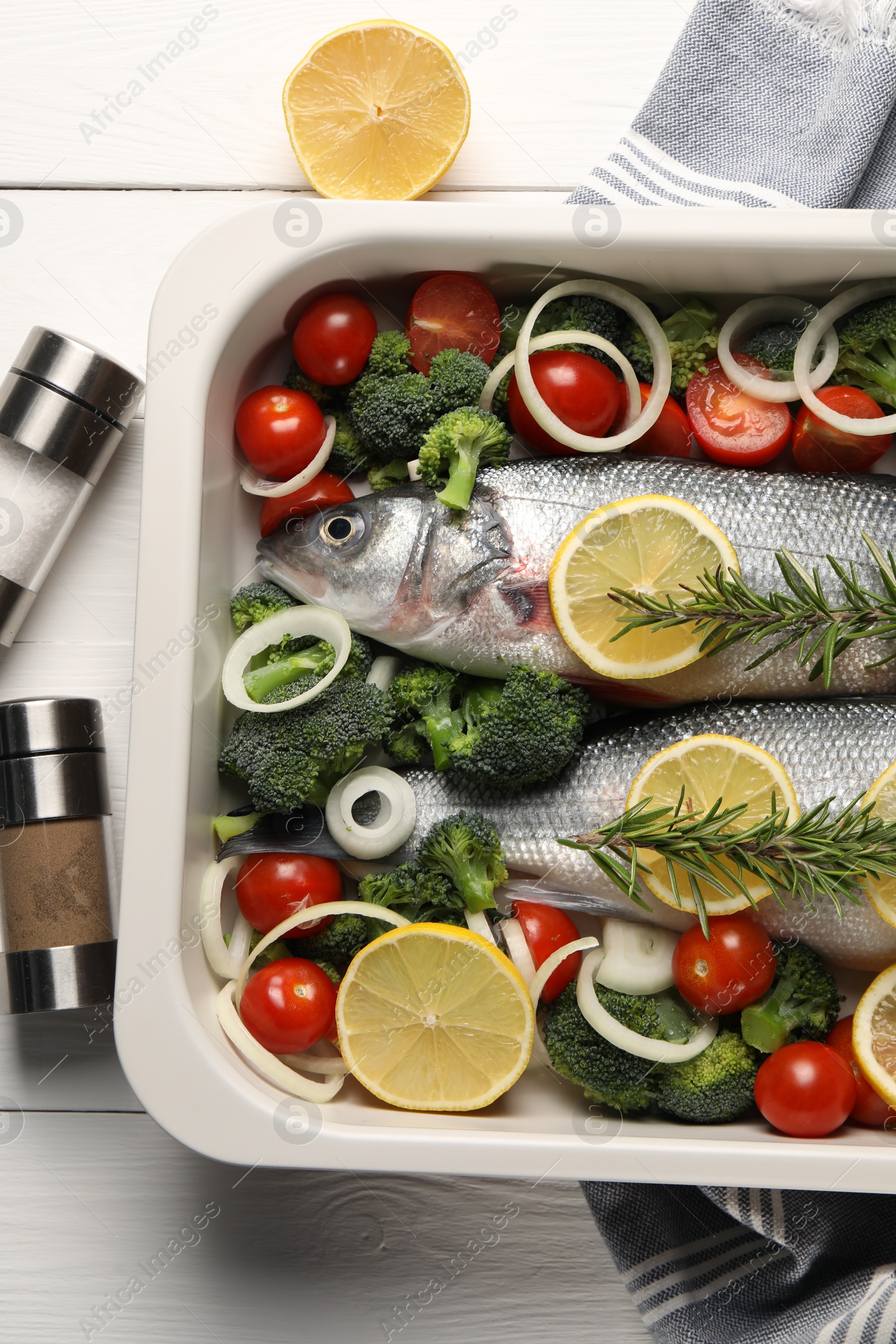 Photo of Raw fish with vegetables in baking dish and lemon on white wooden table, flat lay