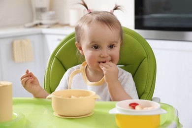 Photo of Cute little baby eating food in high chair at kitchen