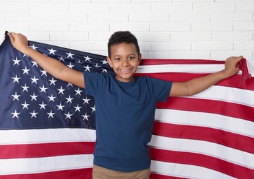 Photo of Happy African-American boy holding national flag near white brick wall