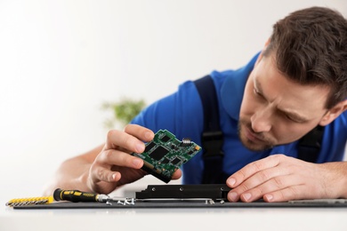 Photo of Male technician repairing hard drive at table indoors