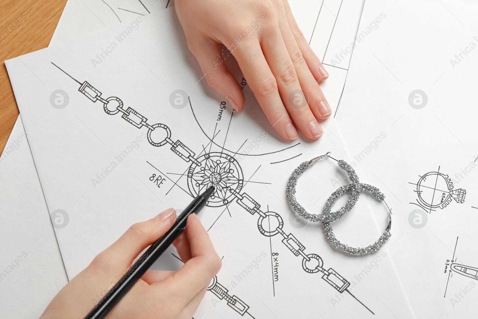 Photo of Jeweler drawing sketch of elegant bracelet on paper at wooden table, top view