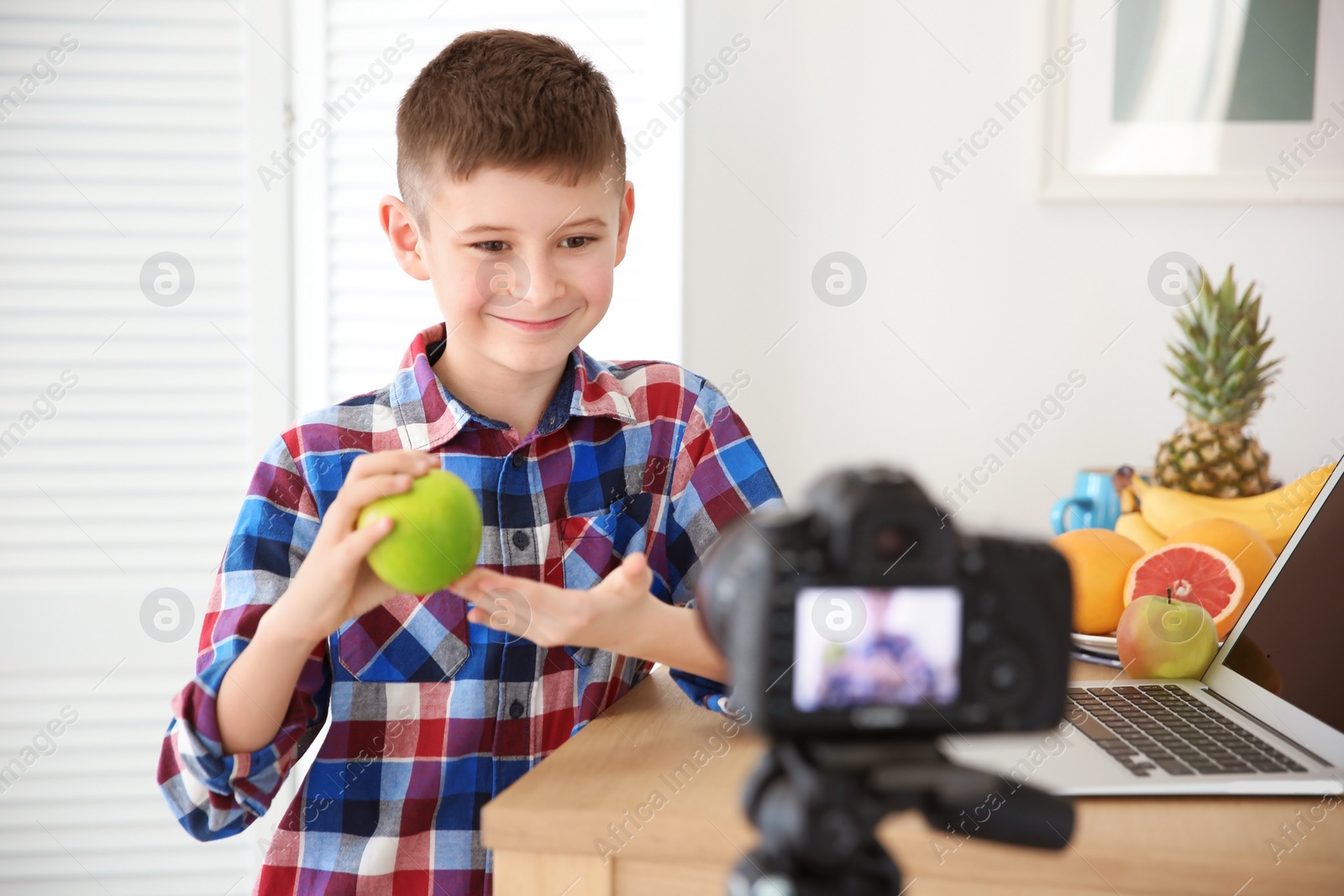 Photo of Cute little blogger with apple recording video at home