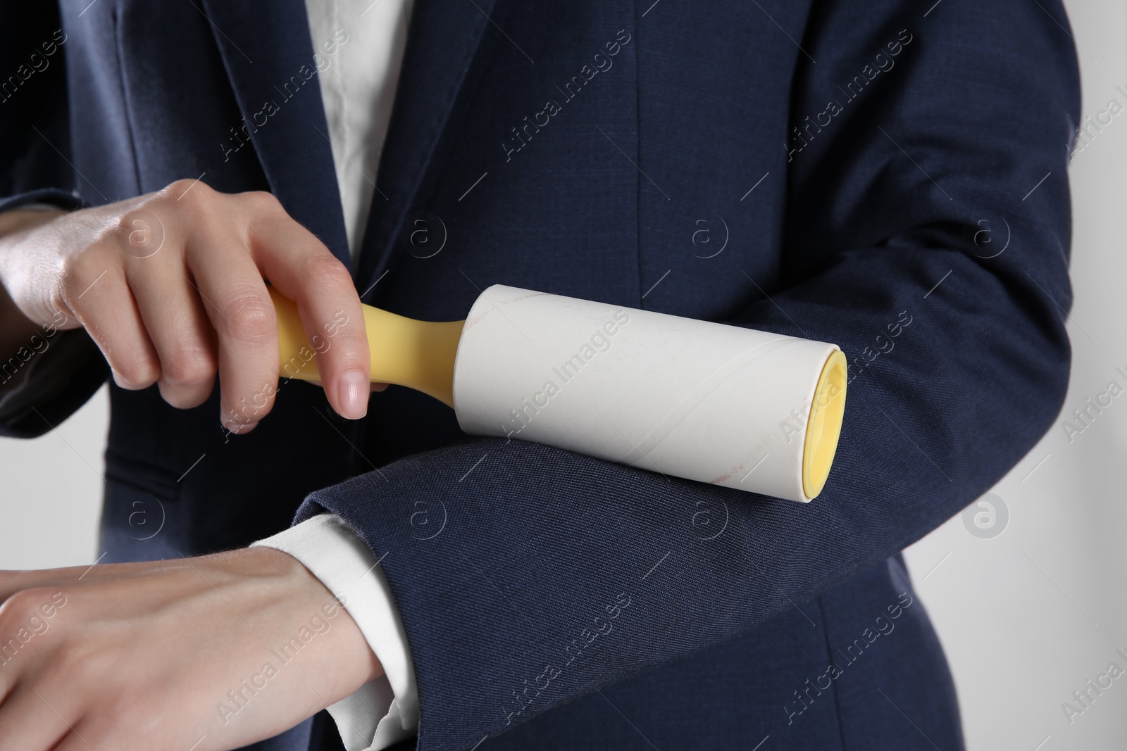 Photo of Woman cleaning dark blue jacket with lint roller on grey background, closeup