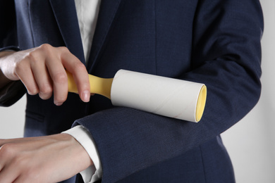 Woman cleaning dark blue jacket with lint roller on grey background, closeup