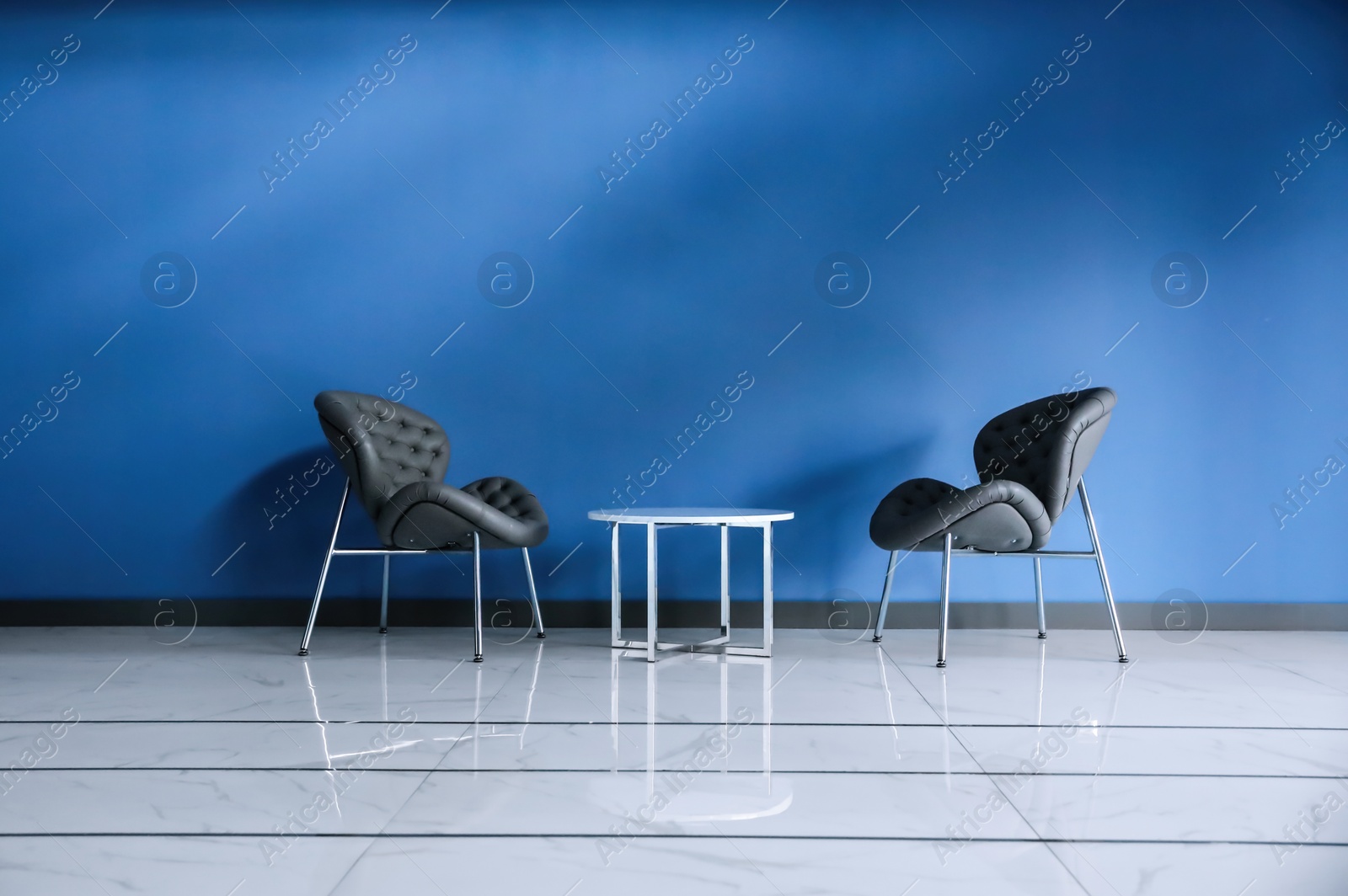 Photo of Comfortable armchairs and metal table near blue wall. Modern room interior