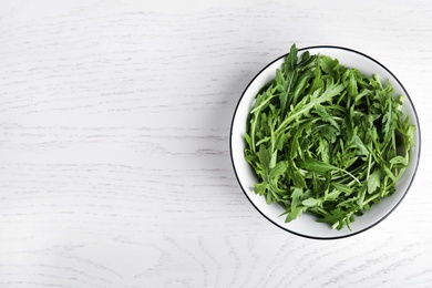 Photo of Fresh arugula in bowl on white wooden table, top view. Space for text