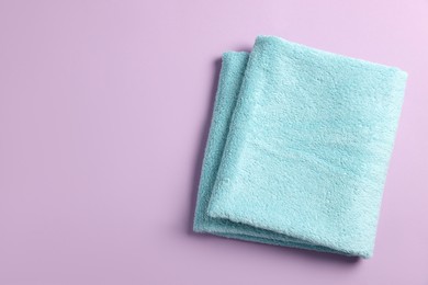 Photo of Soft folded light blue towel on violet background, top view. Space for text