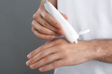 Photo of Man applying cream from tube onto hand on grey background, closeup