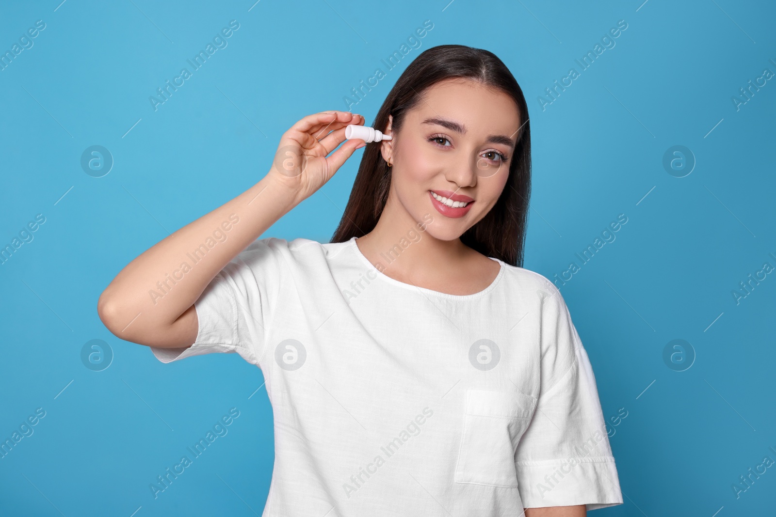 Photo of Young woman using ear drops on light blue background