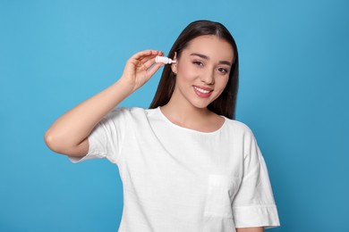 Young woman using ear drops on light blue background