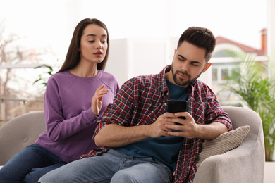 Photo of Distrustful young woman peering into boyfriend's smartphone at home