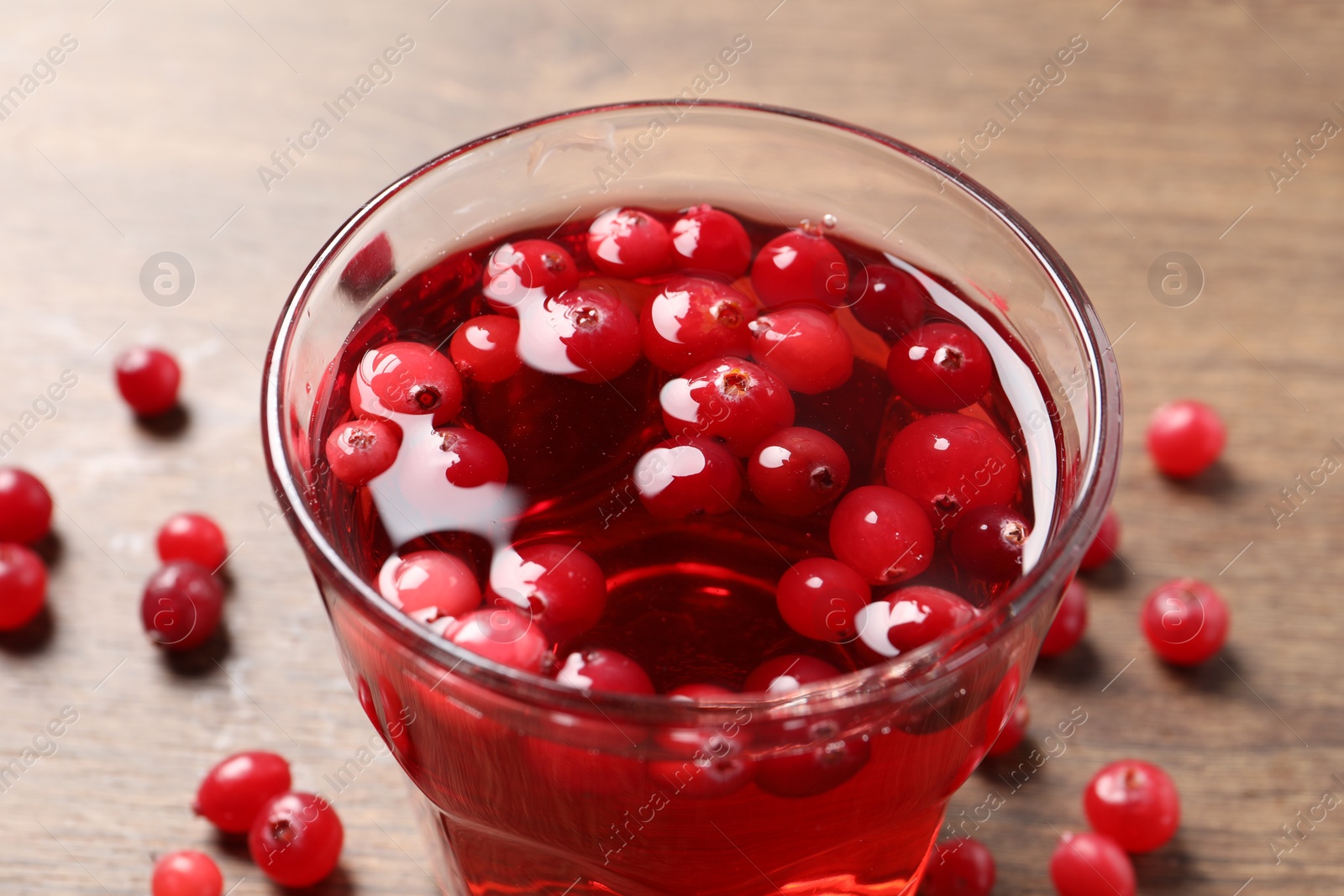 Photo of Tasty cranberry juice in glass and fresh berries on wooden table, closeup