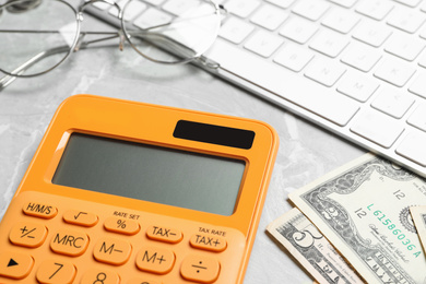 Photo of Calculator, glasses, keyboard and money on marble table, closeup. Tax accounting