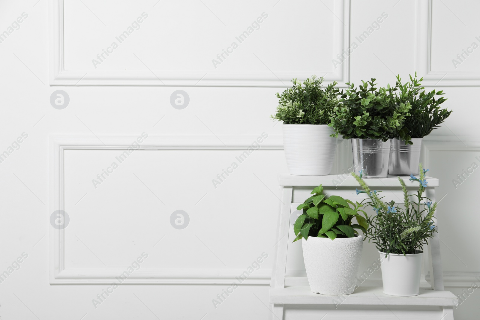 Photo of Different artificial potted herbs on stand near white wall, space for text