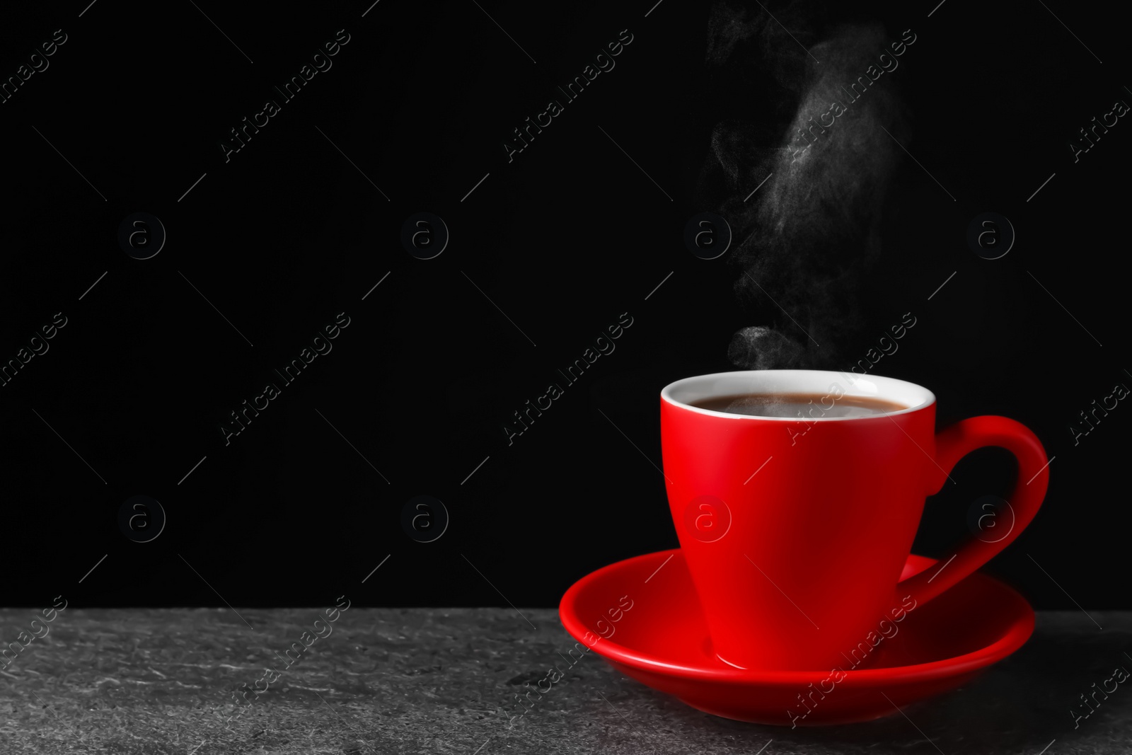 Image of Red cup with hot steaming coffee on grey table against black background, space for text