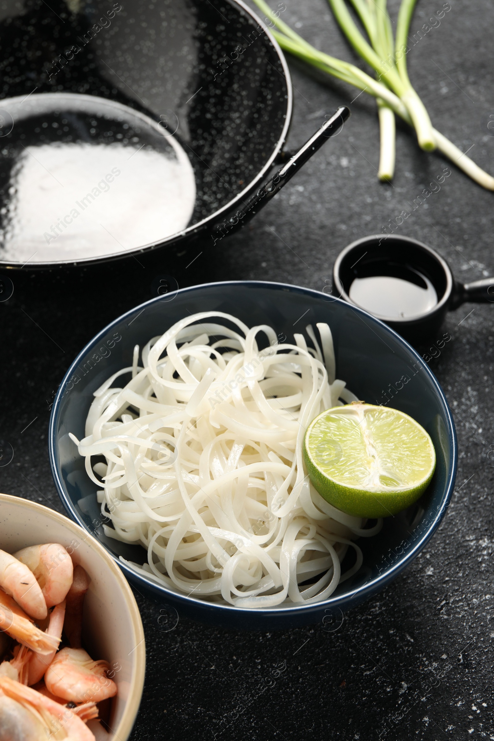 Photo of Noodles, lime and black wok on grey textured table, closeup