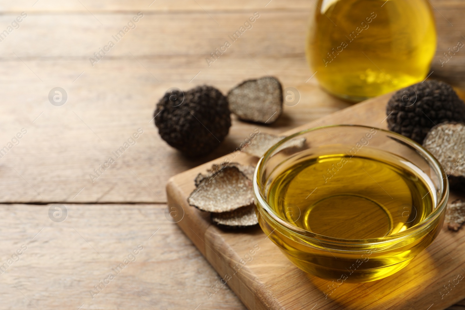 Photo of Glass bowl of truffle oil with board on wooden table. Space for text