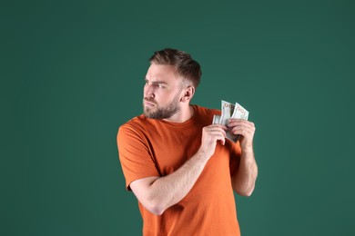 Greedy young man hiding money on green background