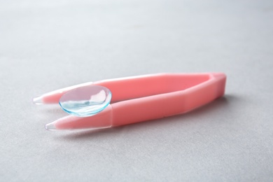 Photo of Tweezers with contact lens on light background