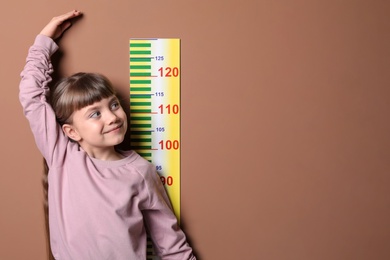 Photo of Little girl measuring her height on color background