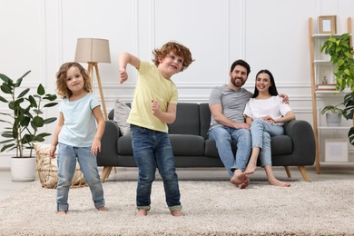 Photo of Happy children dancing while their parents looking at them in room