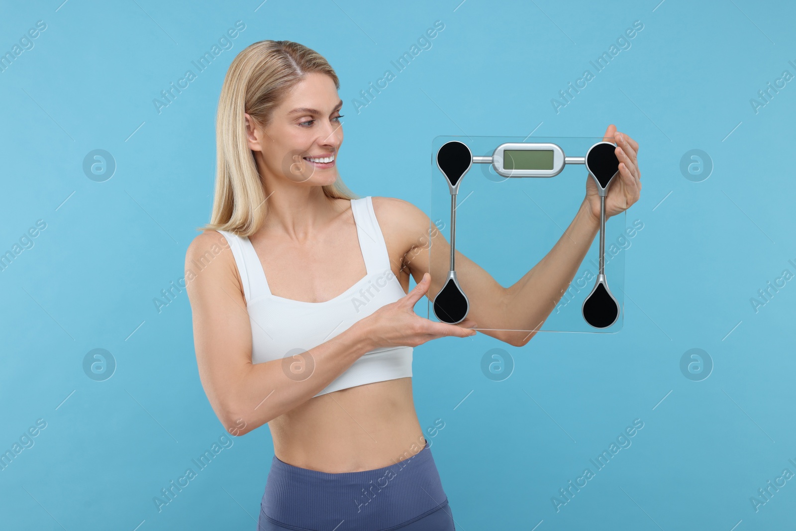 Photo of Slim woman holding scales on light blue background. Weight loss