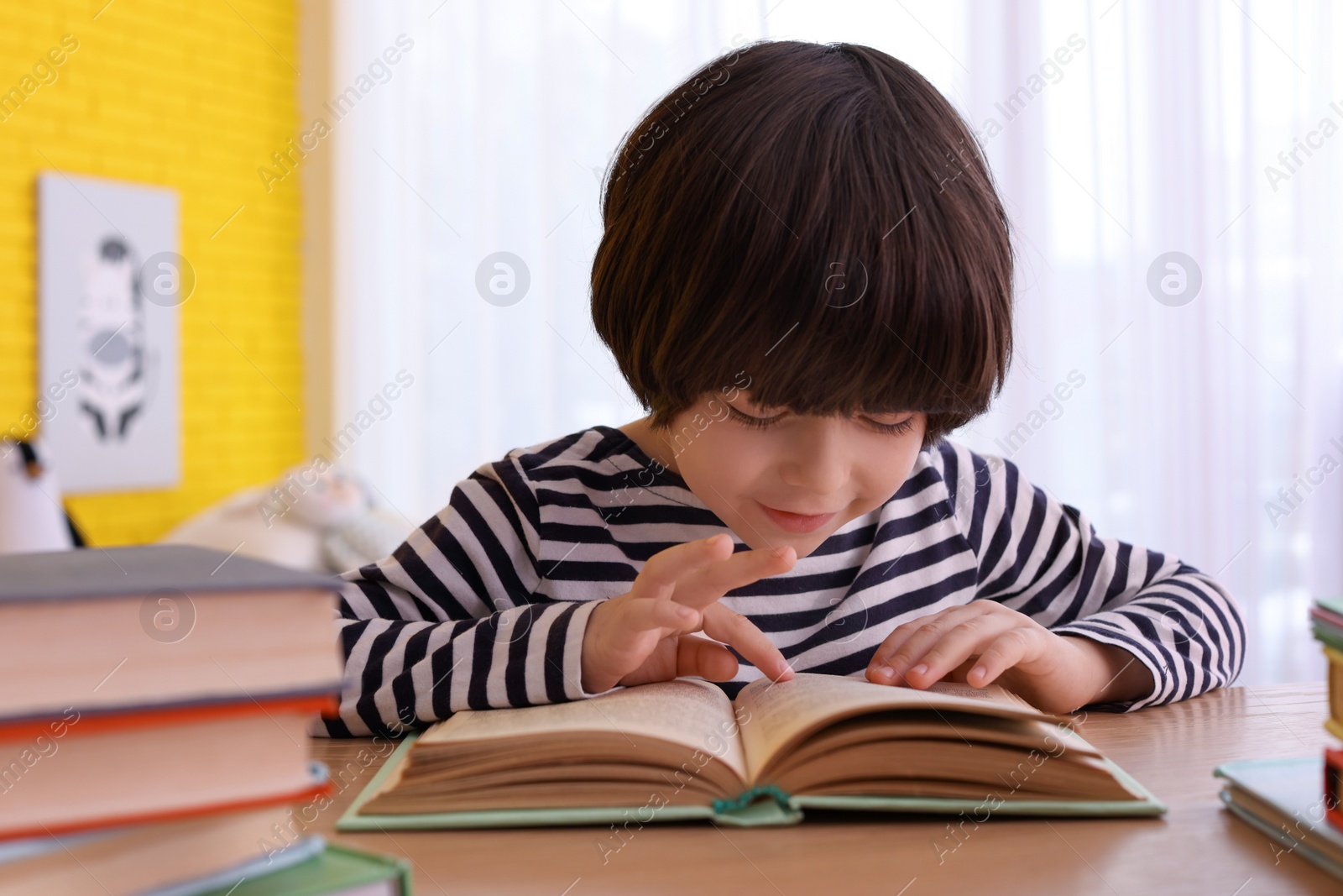 Photo of Cute little boy reading book at table in room