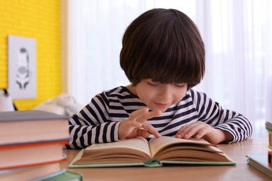 Cute little boy reading book at table in room